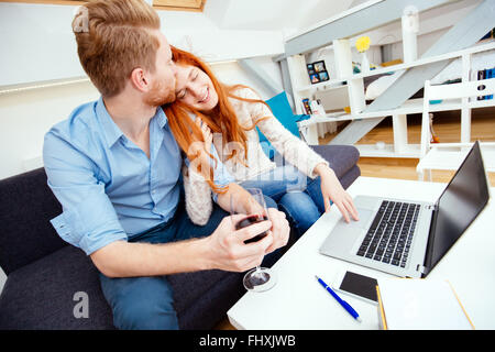 Beautiful couple working on laptop in beau salon, assise sur un canapé Banque D'Images