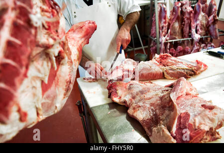 Boucher non identifiables en tablier blanc couper des morceaux de viande à l'aide d'un couteau Banque D'Images