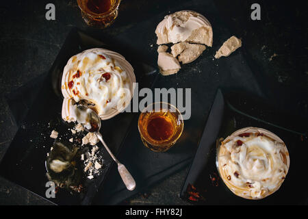 Plaque noire avec commencer à manger de la meringue dessert Pavlova avec sauce au caramel. Avec deux verre de thé chaud sur textile gris serviette o Banque D'Images