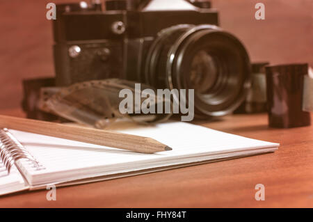 Ancien appareil photo reflex sur la table à côté de la bande de film négatif, et au premier plan un carnet et un crayon. Selective focus sur le crayon. Banque D'Images