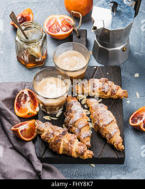 Style Italien accueil petit déjeuner. Café Latte croissants aux amandes et oranges sur sanglant rouge en bois servant de sélection sur le béton Banque D'Images