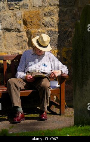 Vieil homme s'endormir tout en lisant sur un banc. Banque D'Images