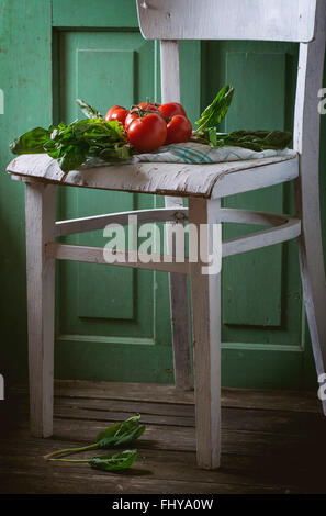 Botte d'épinards frais et les tomates sur la vieille chaise en bois blanc avec mur en bois vert à l'arrière-plan. Banque D'Images