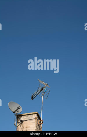 Antenne TV numérique et une parabole sur une cheminée contre un ciel bleu. Banque D'Images