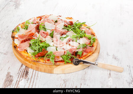 Pizza culinaire avec prosciutto, tomates et fines herbes sèches sur planche à découper en bois sur la table en bois. Banque D'Images