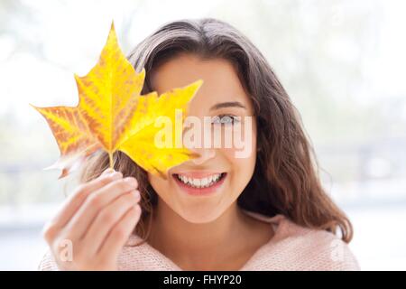 Parution du modèle. Mid adult woman holding an autumn leaf en face de son visage. Banque D'Images