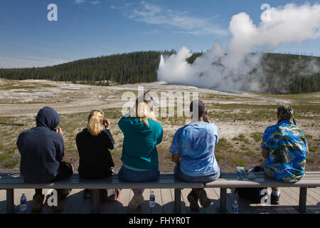 Les visiteurs Old Faithful Geyser qui éclate à l'heure de l'envoi jusqu'à 8 400 gallons d'eau bouillante 184 pieds en l'air - Banque D'Images