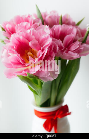 Tulipes roses dans vase blanc avec ruban rouge sur fond whute Banque D'Images