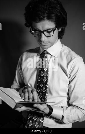 Jeune homme lisant un livre avec des lunettes. Banque D'Images