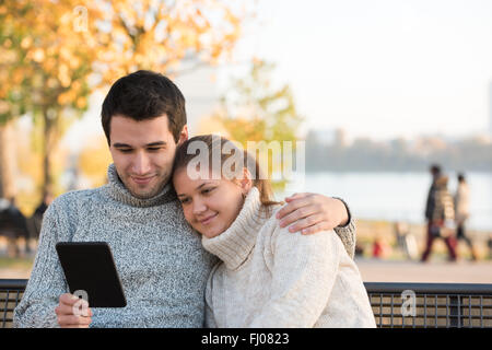 Young couple in autumn park assis sur le banc, la lecture du livre électronique Banque D'Images