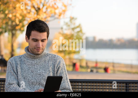 Jeune homme lecture ebook dans le parc Banque D'Images