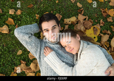 Jeune couple dans le parc, dans l'amour, allongé sur l'herbe verte et des feuilles jaunes Banque D'Images