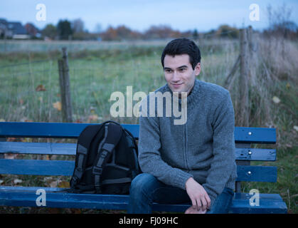 Jeune homme, assis sur le banc à temps le soir, au crépuscule Banque D'Images