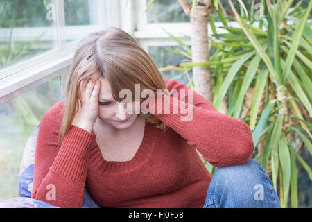 Jeune femme frustrée habillés en pull marron est assise sur le canapé avec sa tête appuyée sur ses mains. Banque D'Images