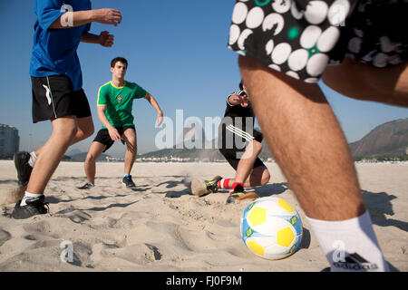 Les jeunes hommes jouent au football à la plage de Botafogo, à Rio de Janeiro, Brésil - mont du Pain de Sucre en arrière-plan. Banque D'Images