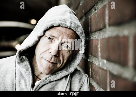 Portrait d'homme portant la veste à capuchon gris appuyé contre un mur de briques Banque D'Images