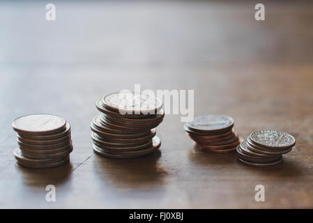 Piles inégales d'entre nous de pièces sur une table en bois Banque D'Images