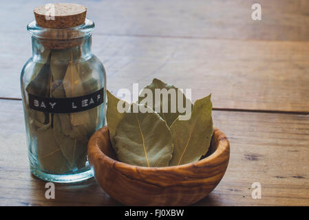 Les feuilles de laurier en pot d'épices en verre et bois d'Olive Bol sur table en bois Banque D'Images