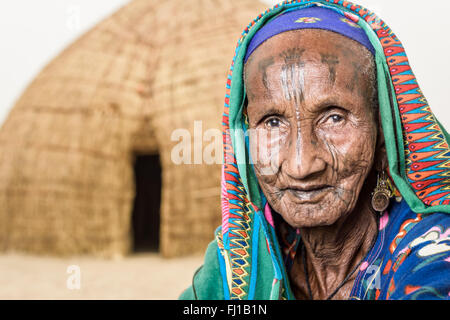 Portrait d'une vieille femme Mbororo typique avec des scarifications sur son visage en s'asseyant sur le sol devant sa hutte. Banque D'Images