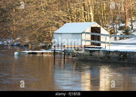 Un petit hangar à bateaux de fortune abandonnées sur la rivière. La neige au sol. Banque D'Images