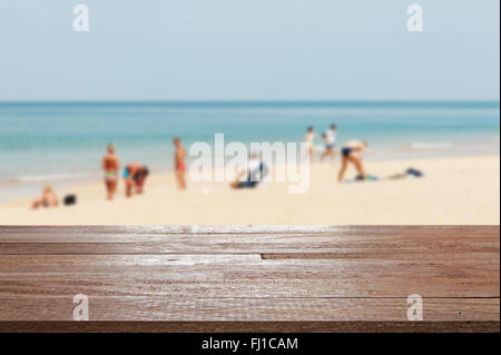 Table en bois sur la mer bleue floue et plage de sable blanc avec certaines personnes - peut être utilisé pour l'affichage ou un montage de vos produits Banque D'Images