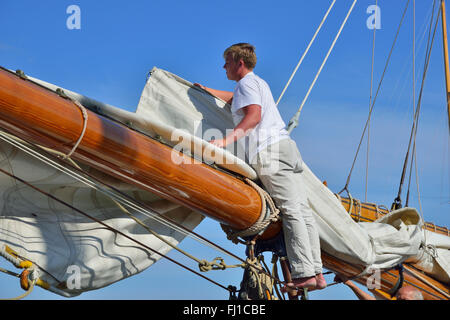 L'équipage du yacht classique en bois grande furls l'énorme grand-voile à la grande flèche en bois dans le port de Cowes, Cowes, île de Wight, Angleterre Banque D'Images