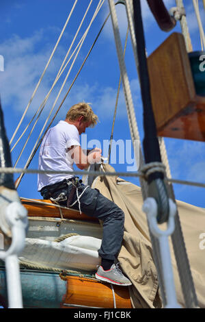 À cheval sur la main de marin travaux de réparation d'une voile à bord d'un yacht classique en bois classique, au cours de la semaine de Cowes, île de Wight, Angleterre Banque D'Images