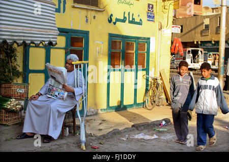 Rue d'Assouan, Egypte - homme est lisant le journal pendant que les enfants marchent et parlent ensemble Banque D'Images