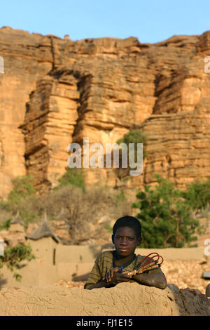 Un garçon pose en haut de maison traditionnelle en pays Dogon, au Mali Banque D'Images