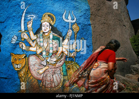 Woman with red saree marche devant une toile de déesse hindoue Durga à Hyderabad , Inde Banque D'Images