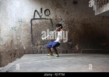 Jeune homme jouer au cricket près de New Market, Kolkata, avec un "non" écrit sur le mur derrière lui. Il rate la balle. Banque D'Images