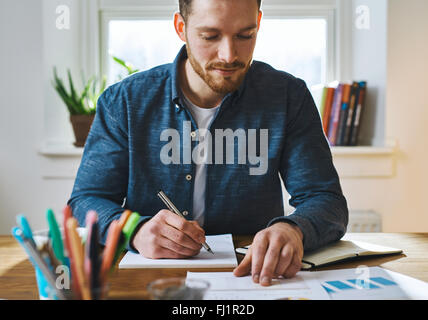 Seul homme barbu en chemise bleue avec le bloc-notes et stylo contrôle de documents pour comparer ou enregistrer de l'information Banque D'Images