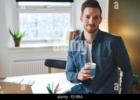 Certain jeune entrepreneur assis dans son bureau à la réception à la recherche dans l'appareil photo Banque D'Images