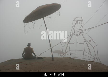 Homme qui prie dans le brouillard en hiver sur ghat de Varanasi, Inde Banque D'Images