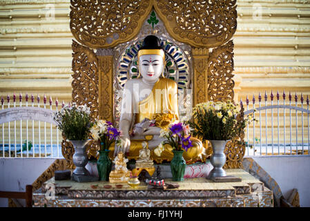 Statue de Bouddha Pagode Kuthodaw Mandalay Myanmar // MANDALAY, Myanmar — Une statue de Bouddha assise et un sanctuaire de dévotion dans le parc de la pagode Kuthodaw, un complexe de temples construit en 1857 sous le règne du roi Mindon. La pagode abrite ce qui est largement connu comme le « plus grand livre du monde », composé du canon bouddhiste Pali complet inscrit sur 729 stèles en marbre. Chaque stèle est logée dans son propre petit sanctuaire appelé kyauksa gu (grotte d'inscription en pierre). Le complexe a été inscrit sur le Registre mémoire du monde de l'UNESCO en 2013 pour la préservation de l'intégralité du Tripitaka sous forme de pierre. Ku Banque D'Images