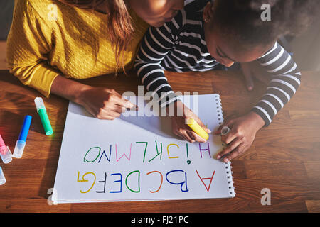 Vue de dessus de petite fille l'apprentissage de l'alphabet à l'aide de crayons de couleur Banque D'Images