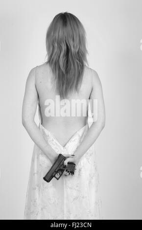 Jeune femme rousse (19 ans) dans une jolie robe de soirée dos nu tenant un pistolet. Banque D'Images