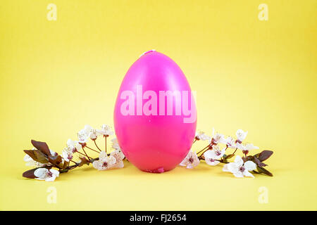 Bougie rose oeuf et brin de fleurs blanches sur fond jaune Banque D'Images