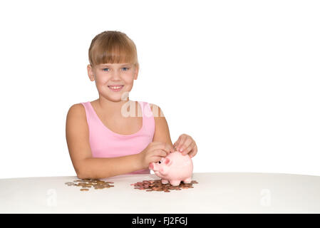 Smiling girl putting coins in piggy bank isolé sur la table Banque D'Images