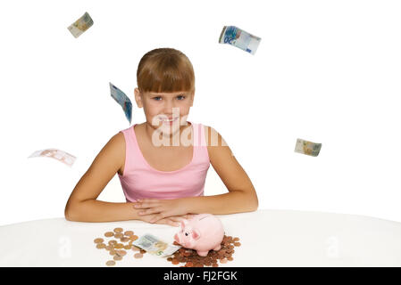 Happy little girl sitting on table avec tirelire et battant isolé autour de l'euro Banque D'Images