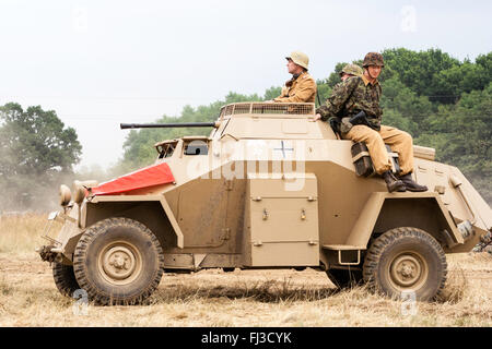 Seconde guerre mondiale re-enactment. L'Afrique allemande Korps Sdkfz 222 voiture blindée, avec le drapeau nazi sur drapé devant et soldats à cheval sur le côté, en passant par. Banque D'Images