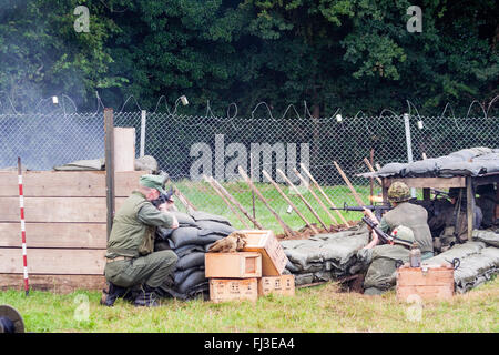 La guerre et la paix, l'Angleterre. Reconstitution de la guerre du Vietnam. Base de feu américain attaqué par ennemi invisible dans les bois, les soldats derrière le fil de feu. retour Banque D'Images