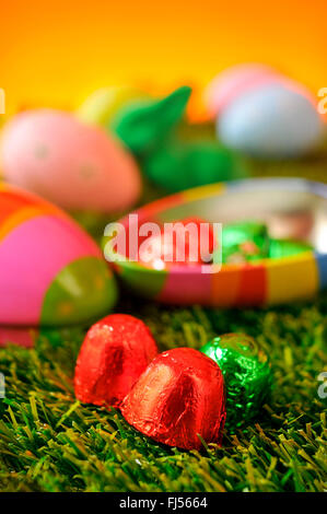 Libre de quelques chocolats enveloppés dans du papier d'aluminium de différentes couleurs, une boîte en forme d'œuf, un lapin de pâques vert et quelques oeufs décorés Banque D'Images