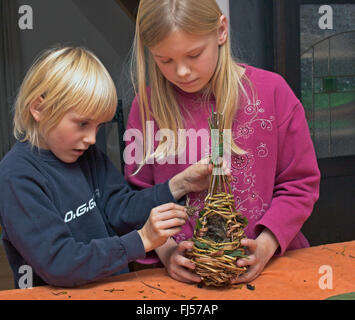 Le matériel du nid pour balle nid, deux enfants tressage des branches de saule et de revêtement de mousse et de roseaux, Allemagne Banque D'Images