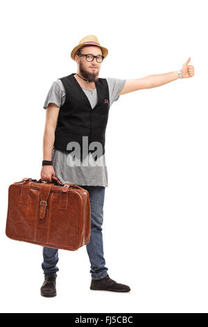 Portrait d'une jeune hipster tenant une valise brune et l'auto-stop avec son pouce isolé sur fond blanc Banque D'Images