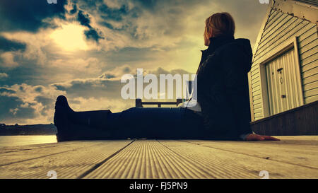 Jeune femme assise confortablement sur plancher cabine de plage en bois Banque D'Images