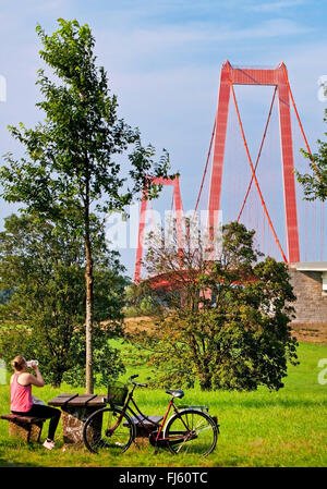 Cycliste féminine ayant une pause devant le plus long pont suspendu traversant le Rhin, l'Allemagne, en Rhénanie du Nord-Westphalie, Bas-rhin, Emmerich Banque D'Images