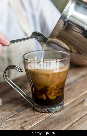 Un café noir. L'on verse du lait dans un café à par un barista. Banque D'Images