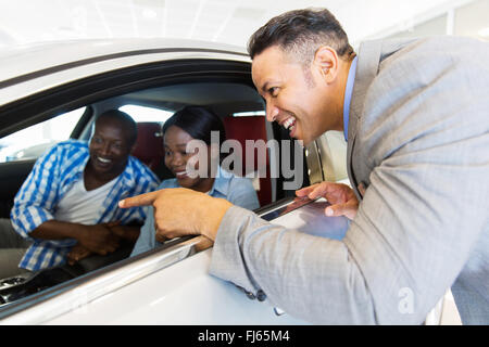 Vendeur de véhicules d'âge moyen montrant nouvelle voiture d'un jeune couple sympathique in showroom Banque D'Images