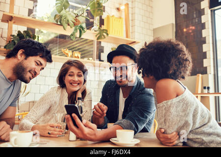 Portrait d'un groupe de jeunes réunion d'amis dans un café et en regardant les photos sur téléphone mobile. Les jeunes hommes et femmes assis à Banque D'Images